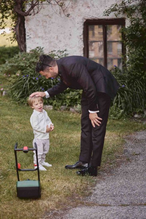 Sposo interagisce con un bambino in un giardino alpino, scatto spontaneo di un fotografo matrimonio Cortina d’Ampezzo.