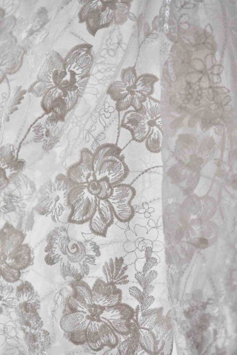 Primo piano del ricamo floreale in pizzo bianco e paillettes di un abito da sposa.