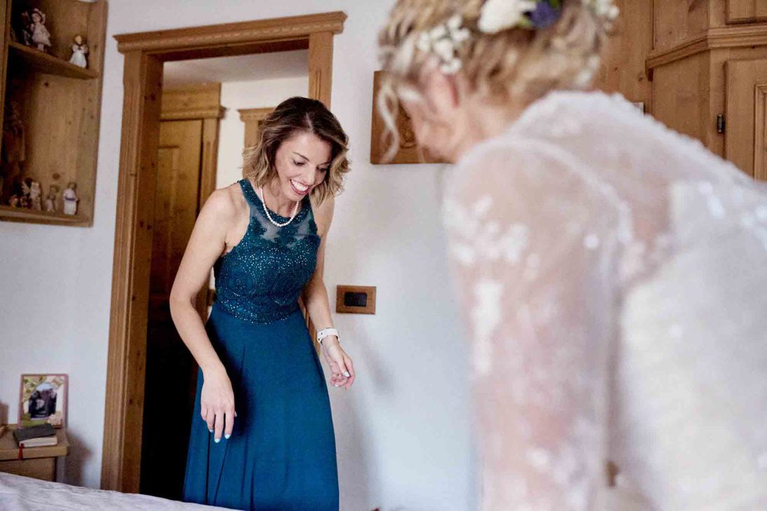 Un'invitata in abito blu guarda con ammirazione la sposa durante i preparativi del matrimonio a Cortina.