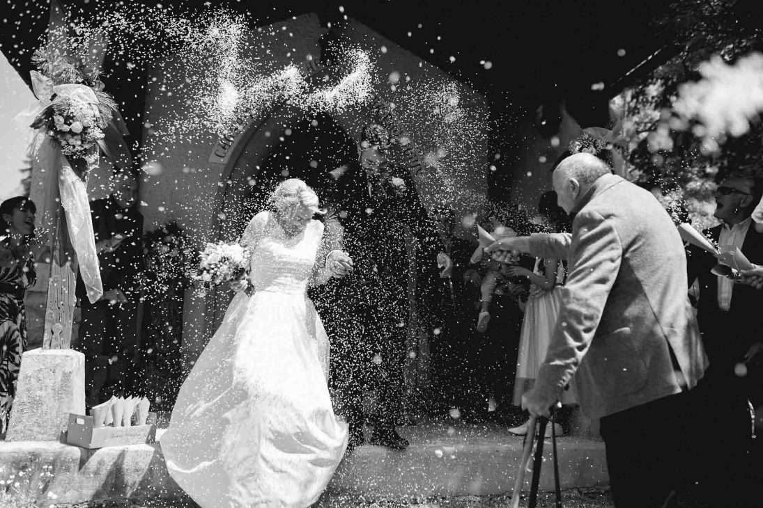 Sposi festeggiati con il lancio del riso all'uscita della chiesa, scatto dinamico di un fotografo matrimonio Cortina d’Ampezzo.