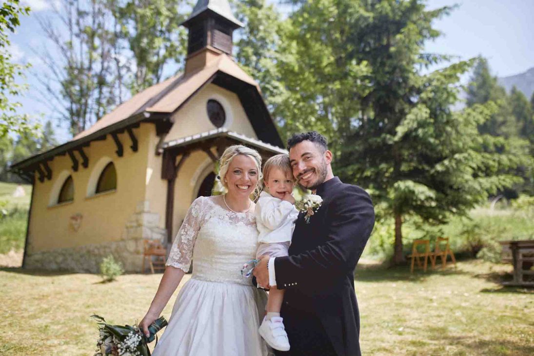 Ritratto di famiglia davanti a una chiesetta alpina curato da un fotografo matrimonio Cortina d’Ampezzo.