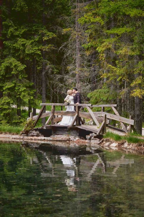 Sposi si baciano su un ponte di legno riflesso nel lago, opera di un fotografo matrimonio Cortina d’Ampezzo.