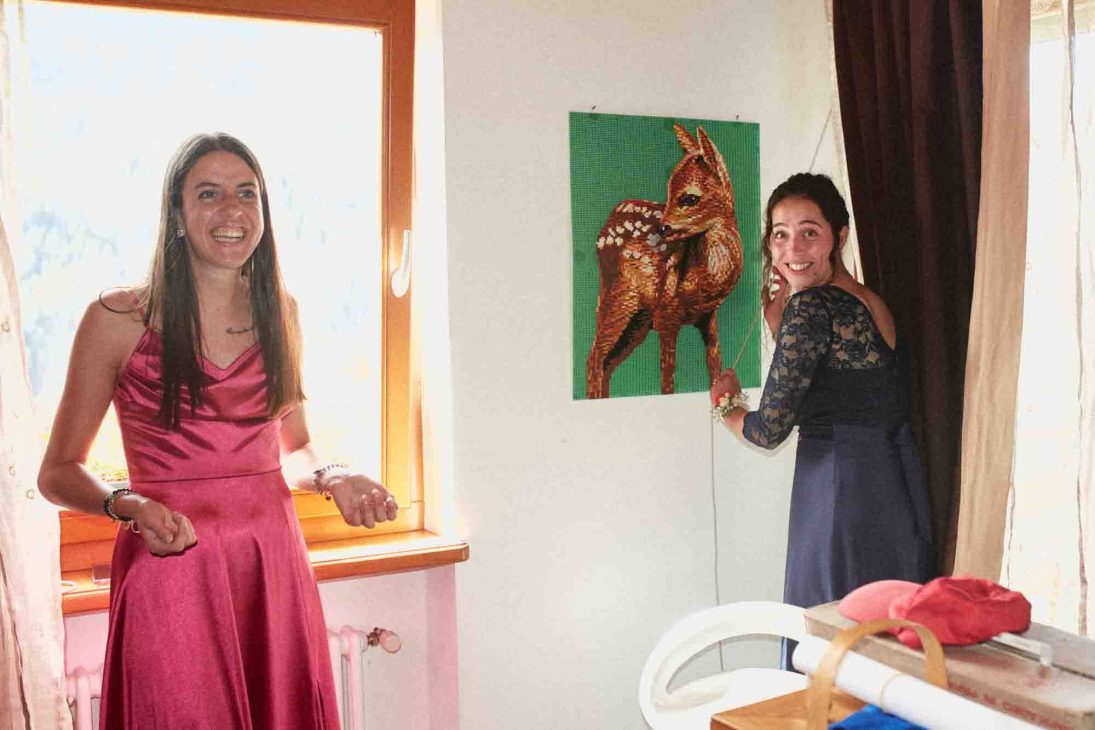Invitata e sposa sorridono accanto a un quadro di cerbiatto, fotografo matrimonio Arabba Livinallongo.