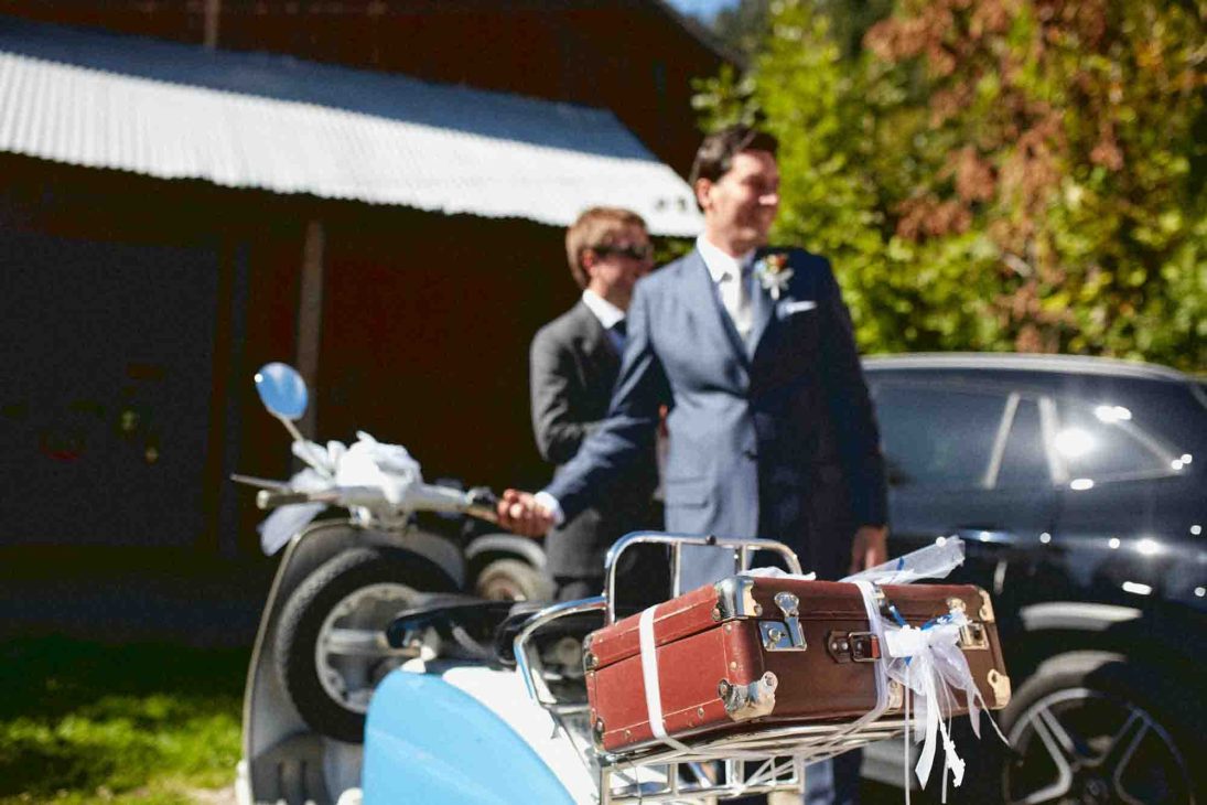 Sposo in abito blu accanto a Lambretta d'epoca con valigia, fotografo matrimonio Arabba Livinallongo.
