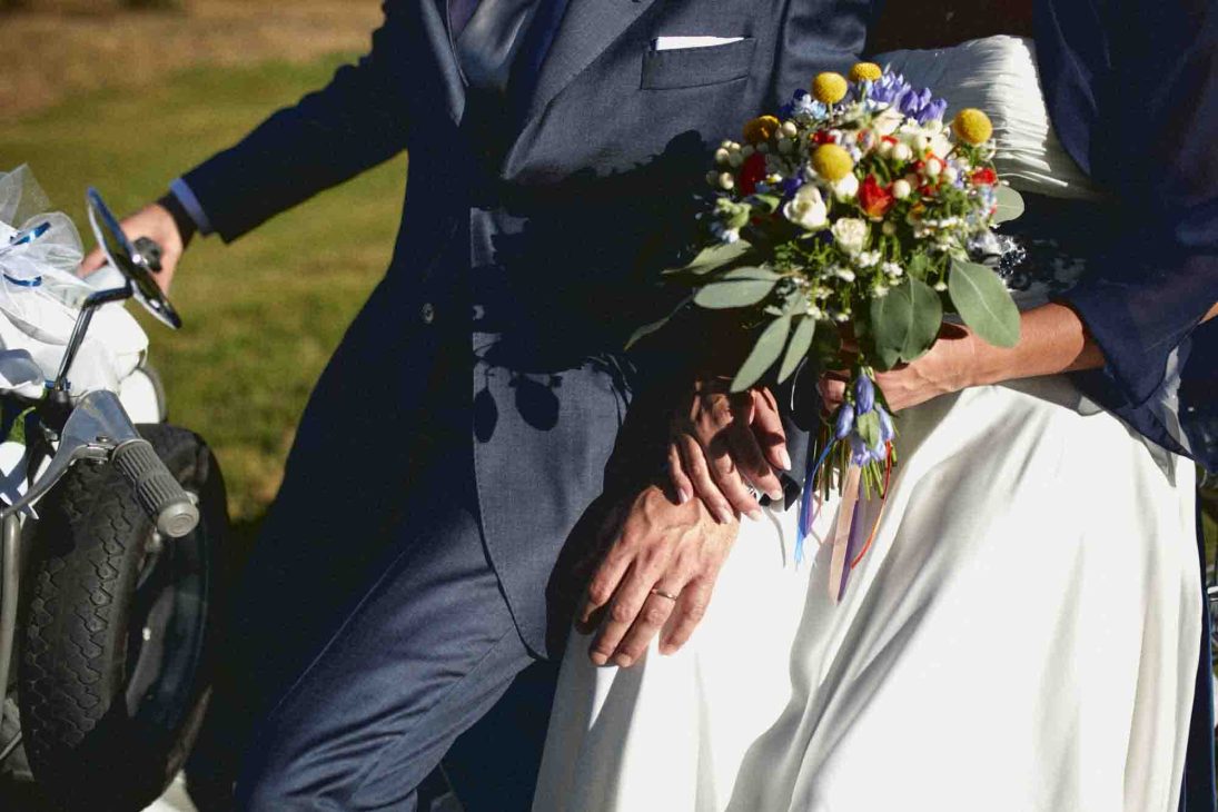 Dettaglio mani sposi con bouquet e Lambretta azzurra, servizio del fotografo matrimonio Arabba - dolomiti.