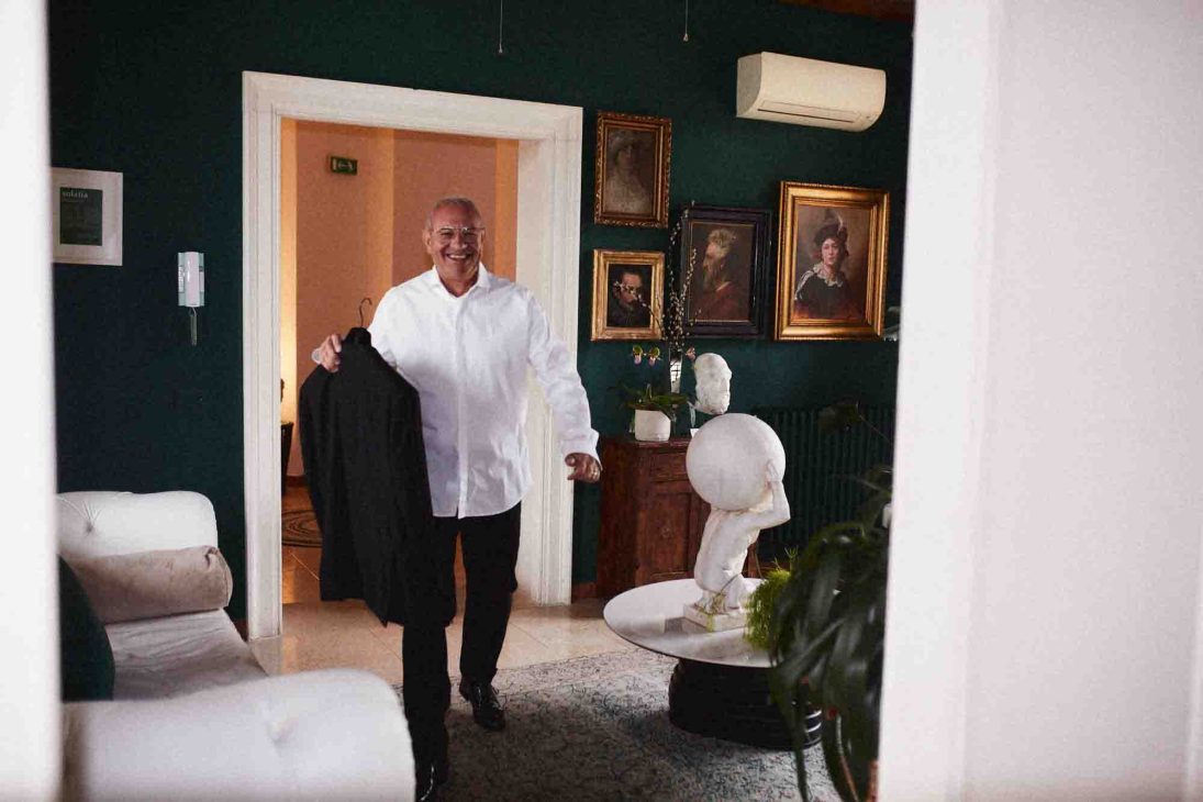 Fotografo matrimonio villa veneta Vicenza: invitato sorridente attraversa una sala elegante con pareti verdi e quadri.