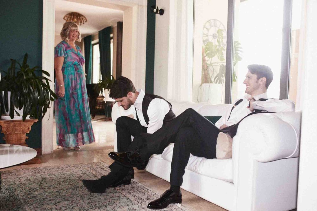 Fotografo matrimonio villa veneta Vicenza: lo sposo e un testimone ridono sul divano durante la preparazione.