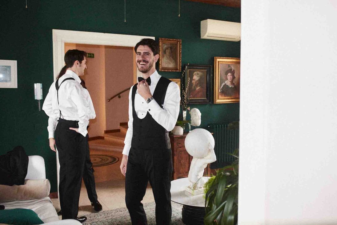 Fotografo matrimonio villa veneta Vicenza: lo sposo in smoking sorride mentre si sistema il papillon in una sala elegante.