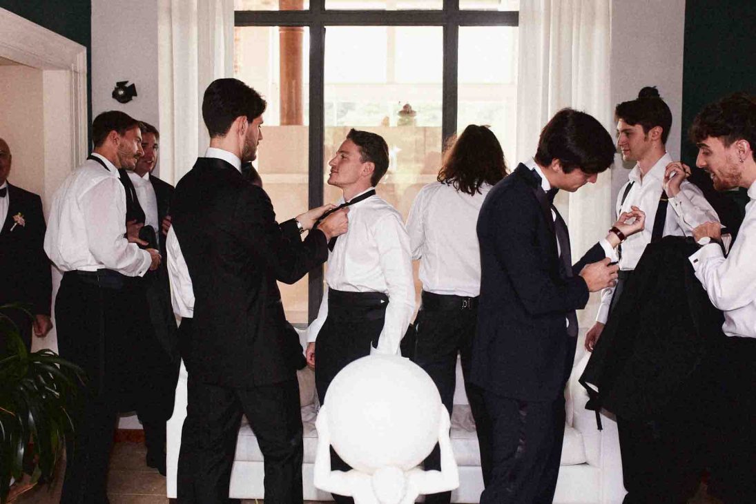 Fotografo matrimonio villa veneta Vicenza: invitati in smoking si preparano in una sala storica con grandi finestre.