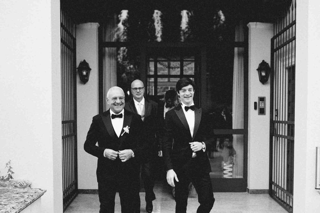 Fotografo matrimonio villa veneta Vicenza: invitati in smoking escono dalla villa sorridendo.