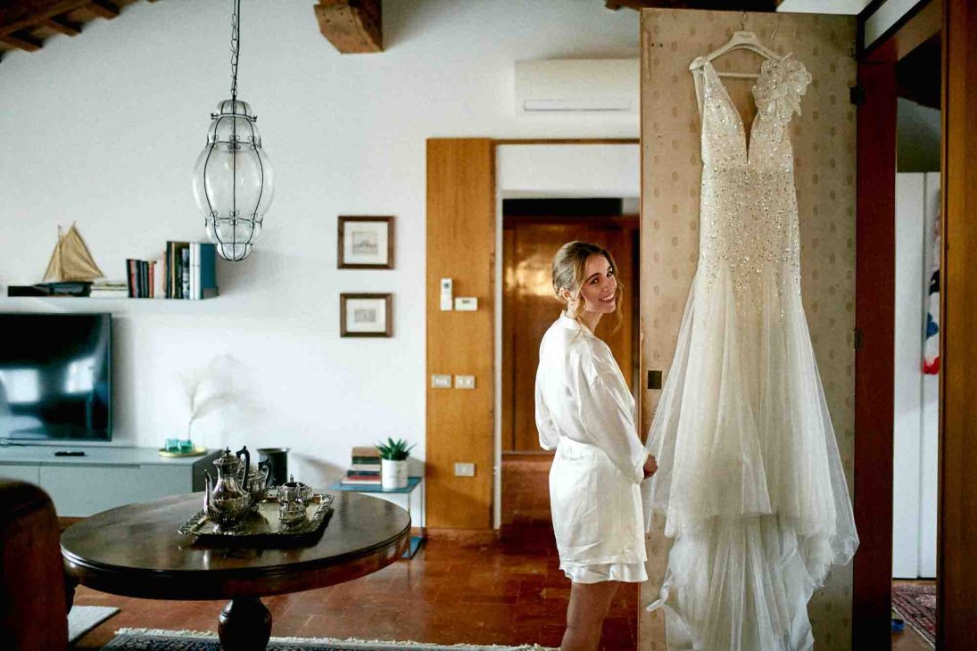 Sposa in vestaglia di seta osserva il suo abito nuziale, scatto di un fotografo matrimonio villa veneta Vicenza.