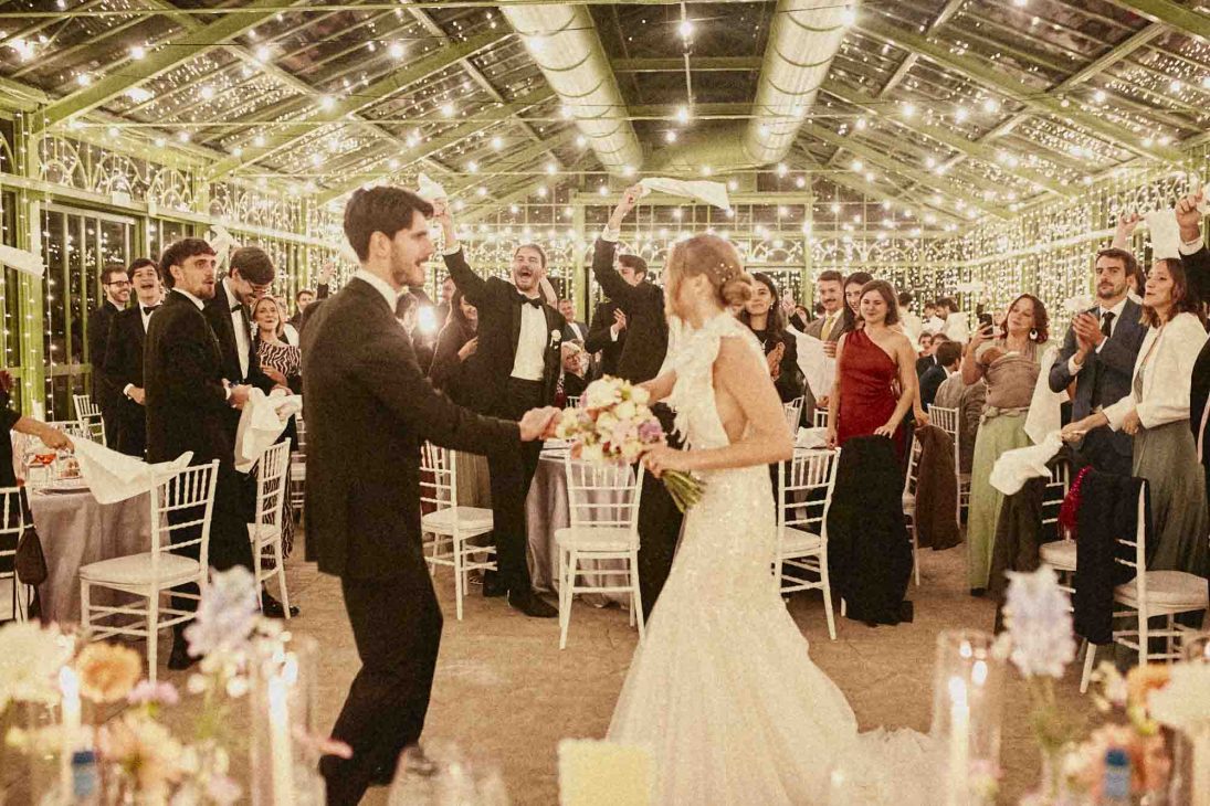 Sposi danzano al ricevimento in una serra illuminata, ospiti sventolano fazzoletti. Fotografo matrimonio villa veneta Vicenza.